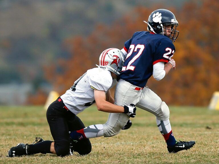 Two athletes in action during an intense outdoor American football game on a grassy field.