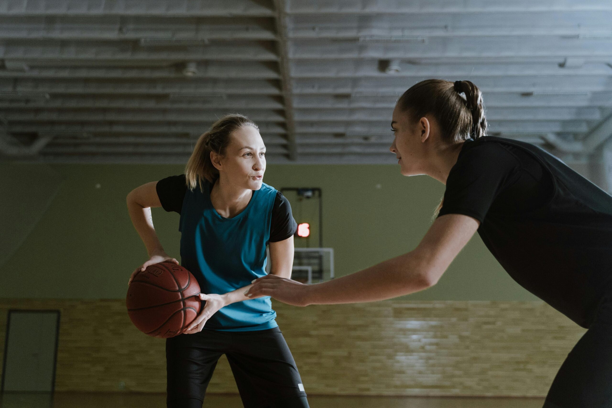 Two women athletes engage in a competitive basketball game indoors.